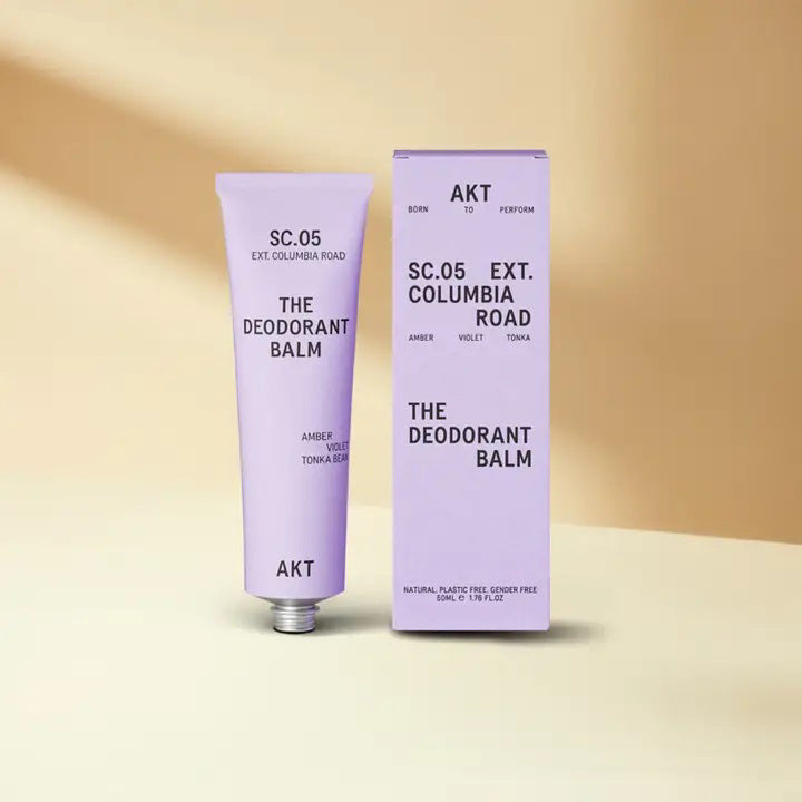 A lavender tube and box of AKT LONDON’s AKT DEODORANT BALM COLUMBIA ROAD rest on a beige surface with soft shadows, highlighting this aluminum-free deodorant balm against a neutral background.