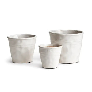 A photograph showcases three CONSERVATORY ORGANIC TAPERED POTS from NAPA HOME AND GARDEN in white ceramic of different sizes. The cachepots feature a slightly textured, uneven surface and a simple, minimalist design. The small planter is positioned in the front center, with the medium and large planters placed behind it, making them perfect for contemporary home decor.