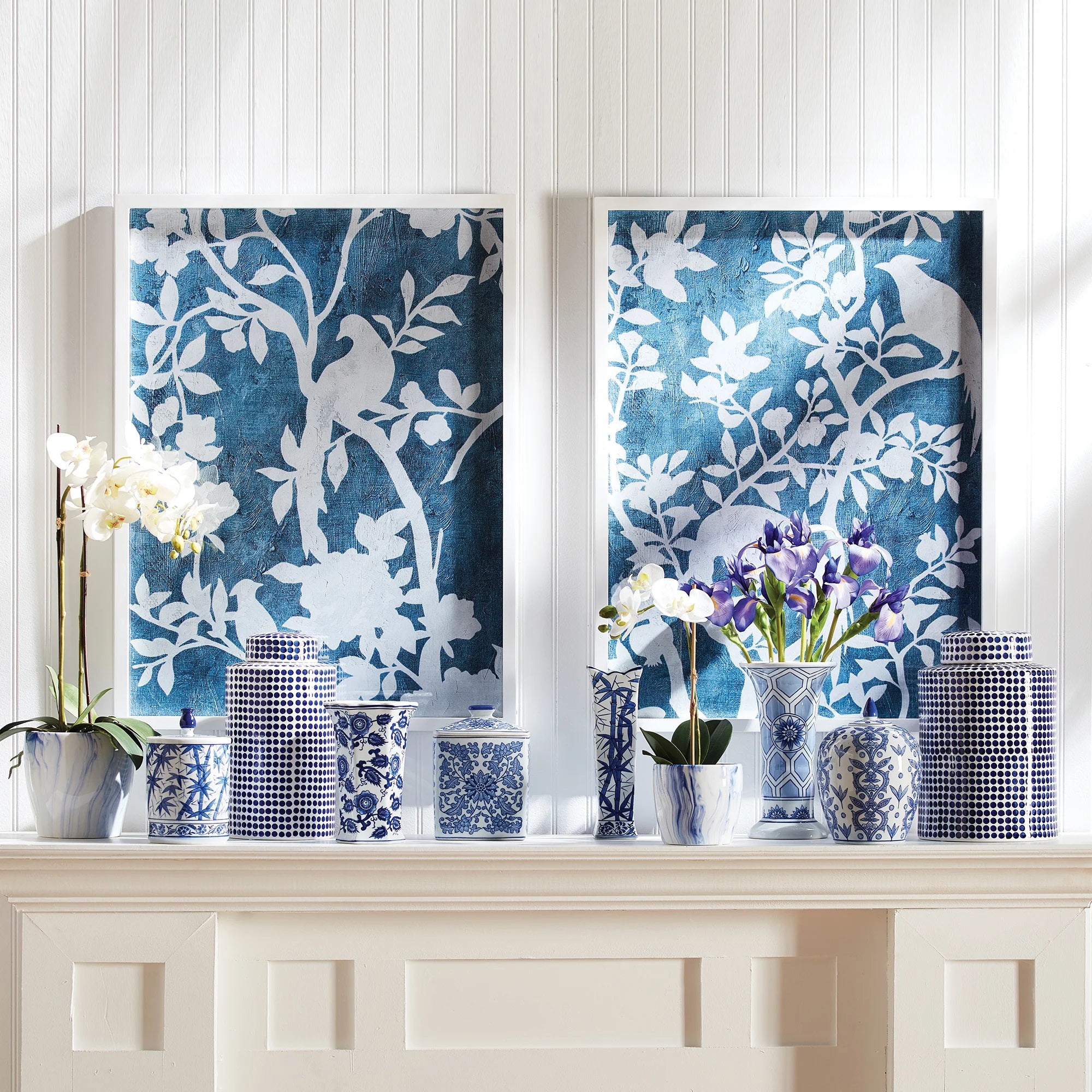 NAPA HOME AND GARDEN's "Aviary Cyano" prints showcase silhouettes of birds on tree branches in a textured blue backdrop, with intricately detailed white leaves and blossoms, offering a serene, nature-inspired aesthetic.