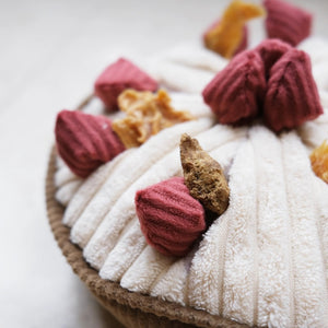 Introducing the LAMBWOLF COLLECTIVE - BERRY PIE DOG TOY, a plush enrichment play object resembling a pie with a quilted crust and topped with fabric strawberries. This round toy features a white filling and has a textured base, designed to imitate a realistic dessert.