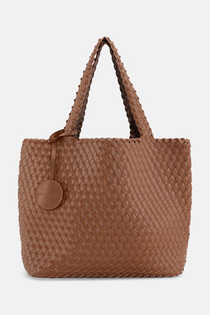 The WOVEN REVERSIBLE TOTE BAG by LINES OF DENMARK is a white tote featuring two shoulder straps and a circular faux-leather tag on one strap. This shopper showcases a textured, interlaced pattern and reversible design, providing stylish and elegant dual styling options. The image background is plain white.