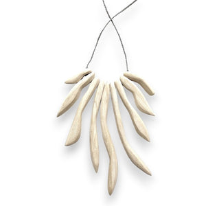 Introducing the ANN LIGHTFOOT - IRREGULAR WHITE WOOD FAN NECKLACE by ANN LIGHTFOOT, featuring a series of elongated, curved white wooden beads strung on a delicate grey cord. The hand-carved wood beads fan out symmetrically, resembling abstract spikes or pendants. Set against a plain white background.