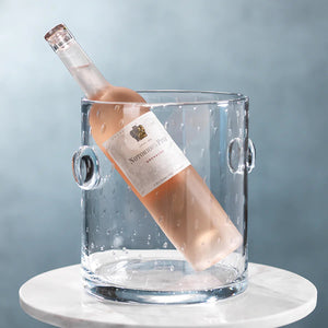 Product Description: The LAGOON BUBBLED ICE BUCKET by ZODAX is a clear, cylindrical glass vessel adorned with small, evenly distributed bubble-like textures. It features protruding circular handles on each side for easy handling. Designed with precise dimensions, the ice bucket boasts a smooth rim and a flat base.