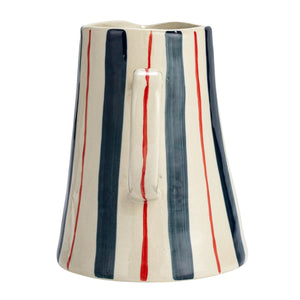 The 2 Quart Stoneware Pitcher with Stripes by Creative Coop features a flared base and a right-side handle. This white ceramic pitcher is adorned with hand-painted vertical stripes in navy blue, red, and white, creating an elegant pattern that covers its entire surface against a plain white background.