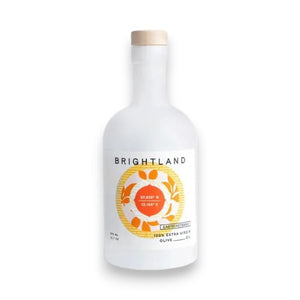 A white glass bottle with a wooden cap labeled "Brightland" and "100% Castelvetrano Olive Oil" in black text. The bottle boasts colorful abstract artwork of hands holding a garlic bulb, capturing the essence of Sicily. This single estate extra virgin olive oil has a net weight of 375 ml / 12.7 fl oz.