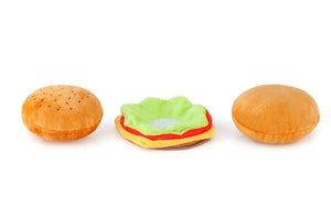 The AMERICAN CLASSIC BURGER by PLAY PET LIFESTYLE, a plush toy shaped like a classic American hamburger, is pictured against a white background. This foodie delight features a soft, brown bun with sesame seeds, green lettuce, a slice of red tomato, yellow cheese, and a brown burger patty.