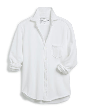 The FRANK AND EILEEN - EILEEN RELAXED BUTTON UP IN TRIPLE FLEECE WHITE features a collared neckline, buttons down the front, and a single chest pocket. The long sleeves are rolled up, and the inside collar label reads "Frank & Eileen EST 1947." With its relaxed fit and slightly curved hem, it exudes a casual, laid-back vibe.