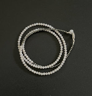 The ANN LIGHTFOOT TRIPLE FACETED MOONSTONE AND PYRITE WRAP BRACELET, resembling a chic necklace, coils in a circle with alternating black and white beads and includes a metal clasp for secure fastening.