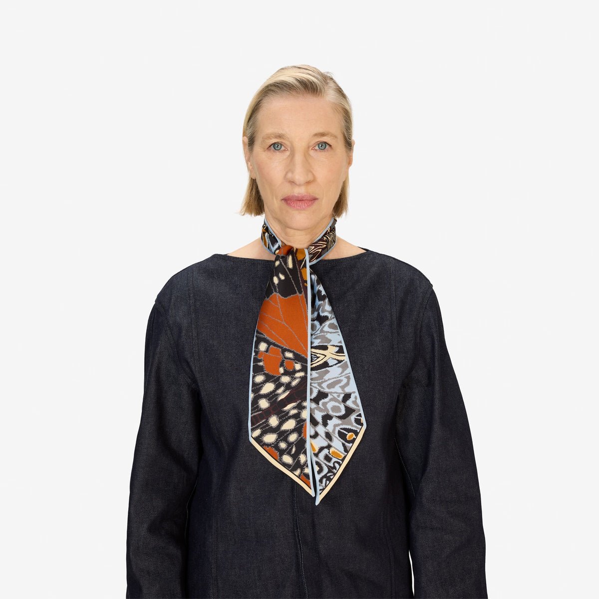 The INOUI EDITIONS - PAPILLON (BUTTERFLIES) SILK RIBBON by INOUI is a double-sided, narrow silk scarf featuring a brown, beige, and cream abstract pattern on one side and a blue, yellow, and gray geometric design on the other.