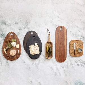 The ACACIA CHEESE BOARD WITH HANDLE by CREATIVE COOP is an oval-shaped cutting board crafted from acacia wood, featuring a smooth, polished surface and natural wood grain patterns. One end of the board includes a handle hole for easy hanging, making it ideal for serving cheese.