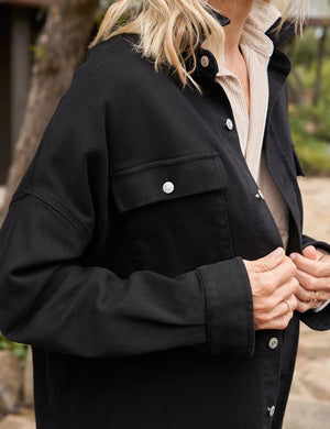 Presenting the Frank & Eileen McLoughlins Utility Jacket: a black, long-sleeve garment with a collared neckline and button-down front. It boasts two chest pockets with button closures and slightly rolled-up sleeves for a touch of California-cool. The label on the inside collar proudly displays "Frank & Eileen," set against a plain, textured white background.