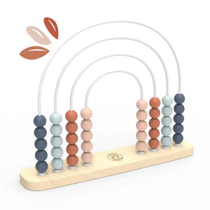 A young child with pigtails is playing with the SPEEDY MONKEY - RAINBOW ABACUS. The abacus, an early educational preschool toy from the SPEEDY MONKEY brand, is made from sustainably sourced wood and features five arcs adorned with colorful beads in shades of pink, blue, and gray. The child, wearing a green shirt and seated indoors against a blurred background, is focused and engaged.