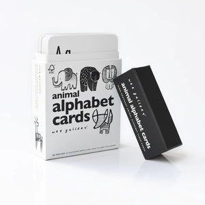 A set of Wee Gallery ANIMAL ALPHABET CARDS is displayed, ideal for children's education. The white box, partially open, reveals some cards inside. Featuring eco-friendly ink and high-contrast nature illustrations of various animals, the box also displays the text "ANIMAL ALPHABET CARDES," with a black lid beside it.