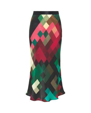 A person is wearing the MIRTO 1956 MULTICOLOR PIXEL PLAID MIDI SKIRT, which boasts a multi-colored, geometric pattern with an elastic satin waistband. They have paired it with a matching long-sleeve top, glittery ankle socks, and high-heeled shoes. The skirt features a vibrant mix of red, green, black, and beige colors that evoke a pixel print design. The background is plain white.