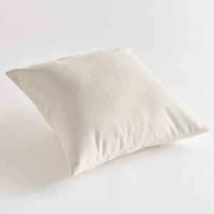 A close-up side view of the COOPER SQUARE INDOOR-OUTDOOR PILLOW 20" by NAPA HOME AND GARDEN against a plain, light background. The image showcases the pillow's white, textured Jacquard fabric and stitching detail, with the zipper partially visible on the edge.