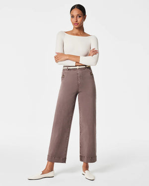 A woman stands confidently with her arms crossed, modeling a long-sleeve white top paired with high-waisted, wide-leg brown SPANX - STRETCH TWILL CROPPED PANTS. She completes the look with white slip-on shoes and is posed against a plain white background, gazing directly at the camera.