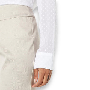 A person wearing a white, long-sleeved, textured blouse with polka dots and a beige skirt. The focus is on the sleeve and part of the waist, highlighting the flattering PULL ON PIQUE ANKLE PANT by KRAZY LARRY, INC, which features a tummy control panel. The background remains plain white.