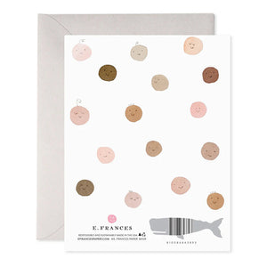 Introducing the "WELCOME BABY GREETING CARD" by E.FRANCES PAPER, featuring a delightful pattern of smiling circles in shades of brown, pink, and beige that resemble faces. A charming whale silhouette enhances the bottom of the design. This card is handcrafted with watercolor accents and is proudly made in the USA. It includes branding details such as "E. Frances," contact information, and a barcode for easy reference.