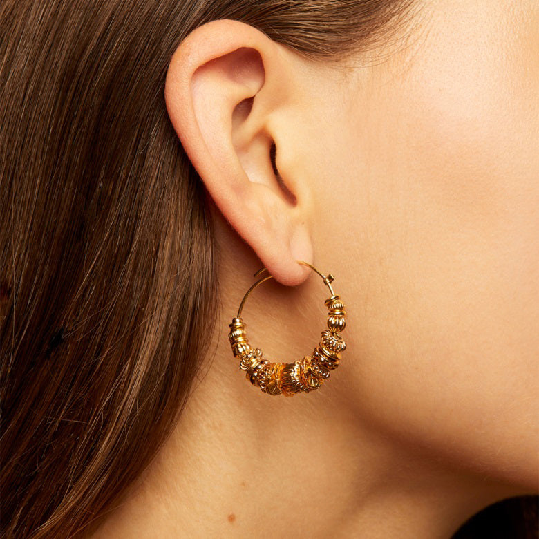 The GAS BIJOUX - ALOHA HOOP EARRING features gold-plated hoops adorned with multiple textured gold beads. Each hoop showcases a central large decorative bead flanked by smaller, intricately designed beads, creating an elegant and intricate appearance. These haute-fantaisie jewelry pieces from Gas Bijoux are set against a white background.