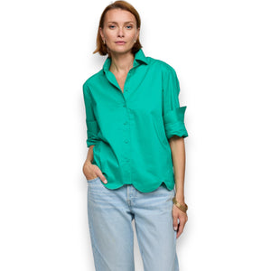 A person with short hair wears a bright green HINSON WU Blaire Scallop Hem Shirt and light blue stretch cotton jeans. One hand is in their pocket, and they sport a bracelet against a plain white background.