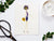 Introducing the CARD CHIC by PETAL PEOPLE PRESS: a whimsical figure crafted from natural materials. This fashionista is adorned in a purple dress with a floral hat made through pressed flower art and holds a small yellow purse. With her long, slender legs, she elegantly poses against a white background.