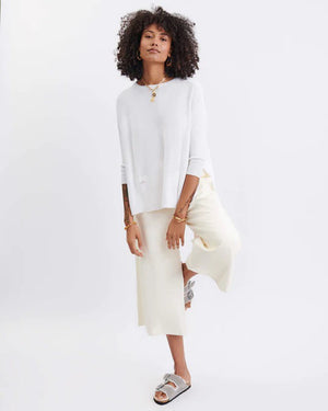 A woman with curly hair smiles while wearing a loose, gray Catalina Crewneck Oversized Sweater by MER SEA. She stands in front of a plain white background.