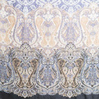 The KINROSS CASHMERE - FADED PAISLEY CASHMERE SILK SCARF by KINROSS showcases an intricate, symmetrical pattern featuring a blend of green and yellow hues on a blue-toned background. The design, reminiscent of ornate, floral, and paisley-like motifs, creates a visually rich tapestry-like appearance that evokes the luxurious feel of woven silk and cashmere.