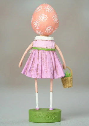 The ESC AND COMPANY - SHELLY FIGURINE by ESC AND COMPANY, INC is a whimsical poly resin piece featuring a girl in a pink dress and headscarf. At 6.25" tall, she holds a basket with green contents on a green base adorned with floral details and wears a surprised expression.