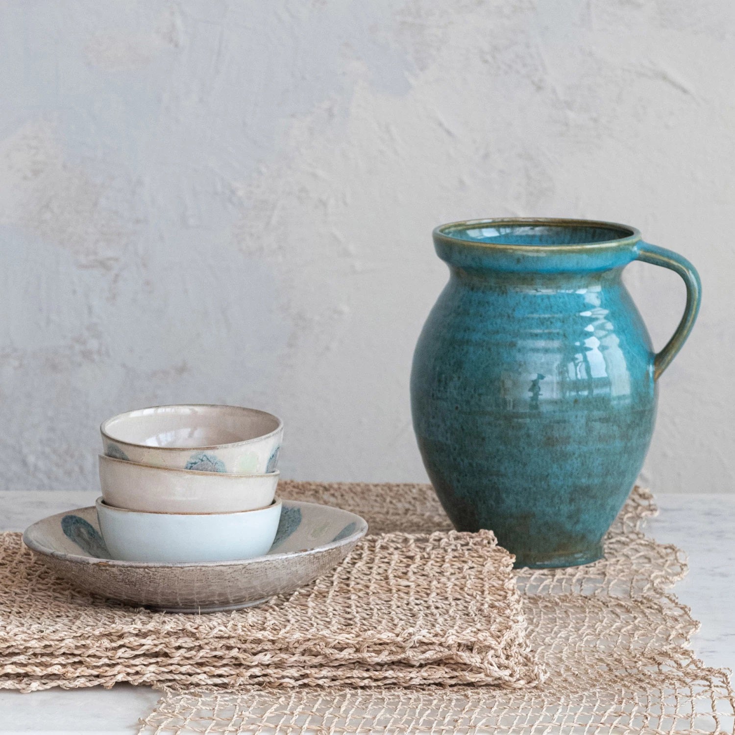 Introducing the 4 Quart Jug with Handle by Creative Coop: This ceramic jug features a glossy turquoise finish. It showcases a rounded body that subtly tapers towards the top, complemented by a wide lip and a single handle on one side. The handcrafted look and glaze variations imbue it with rustic charm, making it both functional and decorative.