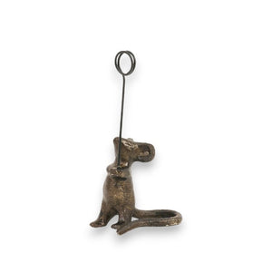 The MOUSE CARD HOLDER by CREATIVE COOP is a charming bronze-colored, cast iron sculpture of a mouse. It stands upright with a vertical metal loop on its tail that is perfect for securing notes or photos, and its distressed finish adds appeal against the plain white background.