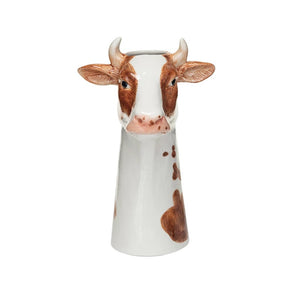 The CREATIVE COOP CERAMIC COW VASE is a hand-painted stoneware vase shaped like a cow's head and neck, featuring a farmhouse style with brown-and-white details, horns, and a realistic expression. Its top opening adds functionality to its captivating design against a plain white background.