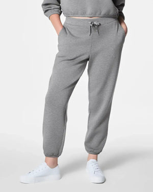 A person wearing SPANX AirEssentials Jogger Pant in Heather Gray with a drawcord waist and hands in pockets. Their top is partially visible, and they are wearing white sneakers against a plain white background, emphasizing the comfort of their attire.