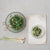 Two RECYCLED GLASS HOBNAIL SERVING BOWLS by CREATIVE COOP sit on a textured surface, one with a mixed green salad and the other with a grain-based salad. Gold scissors rest beside the larger bowl, while three stalks of lemongrass decorate the left.