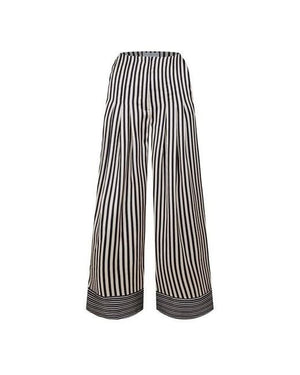 The NEVER FULLY DRESSED - ISLA TROUSER from NEVER FULLY DRESSED features wide-leg pants with vertical black and white stripes, a fitted waist, and a solid black band with white stripes at the bottom. The softly tailored design enhances the leg length, creating a bold and stylish look.