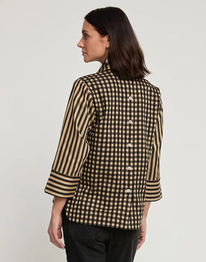 A woman with shoulder-length dark hair wears the HINSON WU - AILEEN 3/4 SLEEVE STRIPE GINGHAM COMBO SHIRT, a black and beige striped blouse featuring a small collar and a partial zip at the front. She pairs it with black pants and stands against a plain white background, one hand in her pocket.