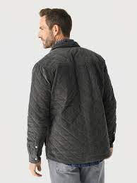 A man with short, curly hair and a beard wears the CRIQUET - CORDUROY QUILTED SHACKET by CRIQUET and blue jeans, standing against a white background while smiling and looking to his right.