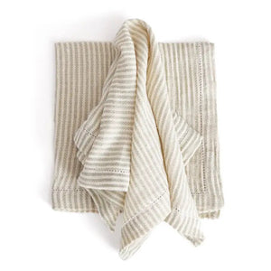 The PRIM NAPKIN by NAPA HOME AND GARDEN offers a neatly arranged set of off-white and beige striped fabric napkins, designed to be machine washable for your convenience. Made from lightweight fabric, these napkins display a simple and elegant pattern of evenly spaced vertical stripes. The set is neatly folded with one napkin draped over the top to showcase their texture and design beautifully.