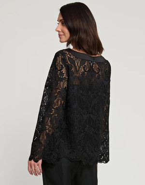 A woman with shoulder-length dark hair is wearing the HINSON WU - BLAKELY LACE TOP, a long-sleeve black lace top that features flared sleeves, paired with black pants. She stands against a plain light gray background, neutrally expressing herself with one hand on her hip.