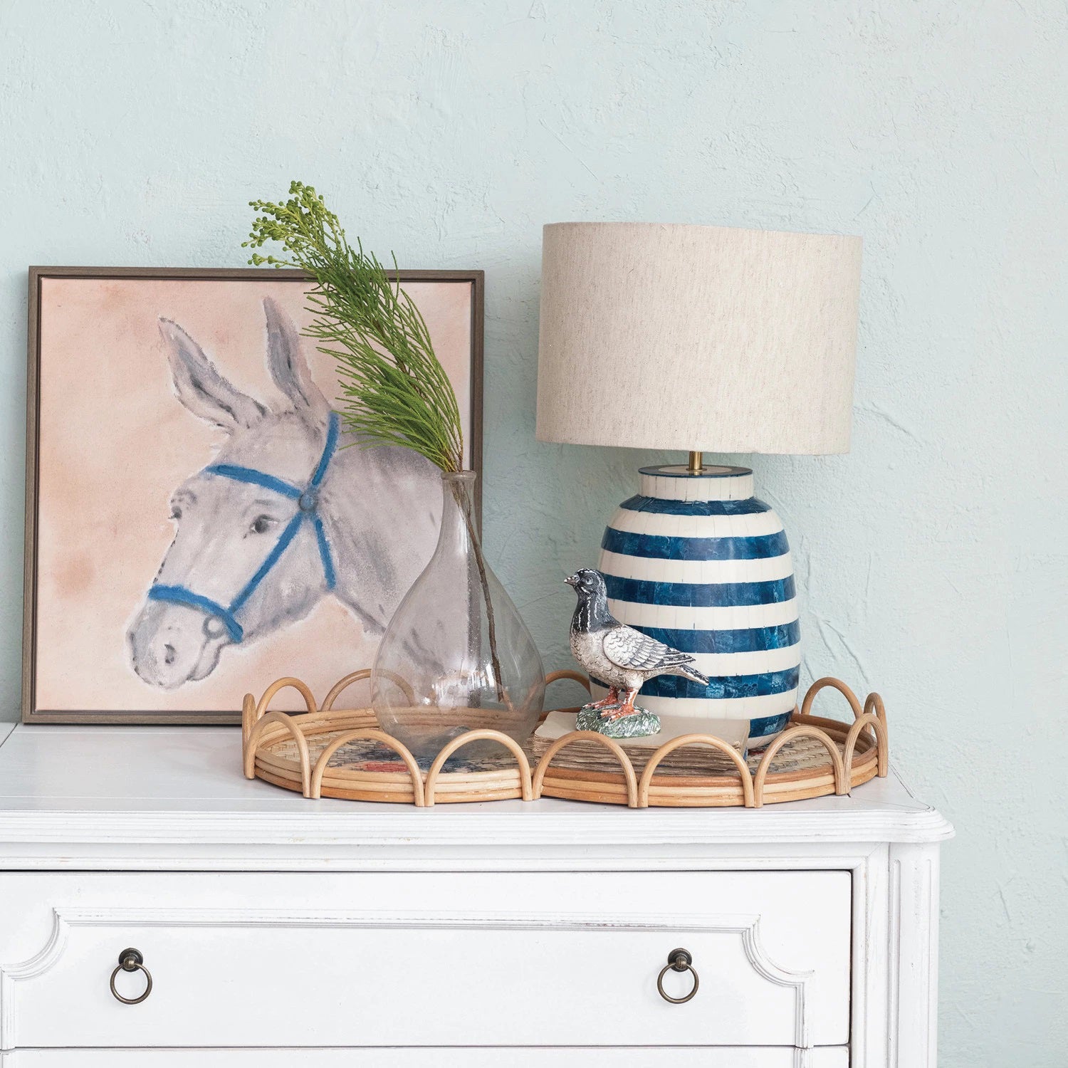 The CREATIVE COOP INLAID TABLE LAMP WITH BLUE STRIPES features a white cylindrical cotton shade atop a round, ceramic base designed with alternating horizontal stripes of white and textured blue, giving it a coastal or nautical feel. This stylish lamp is positioned against a plain white background.