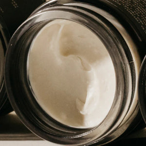 A close-up shot of an open jar filled with PRESTON - CREAM POMADE UNSCENTED. The smooth, frizz-free texture of the pomade is visible within the dark-colored container. The jar is placed on its side against a neutral background.