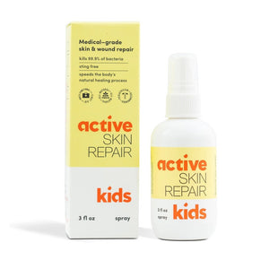 A yellow and white spray bottle labeled "ACTIVE SKIN REPAIR - KIDS SPRAY" is placed next to its matching box. This pediatrician-recommended, medical-grade spray from ACTIVE SKIN REPAIR kills 99.9% of bacteria, is sting-free, promotes natural healing, and serves as a non-toxic first aid spray for effective kids' skincare.