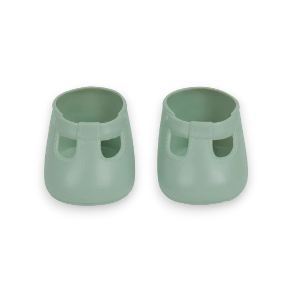 A close-up of a baby wearing OLLI ELLA USA DINKUM DOLL SHOES in Mallow Pink and white socks. The baby is seated on a soft, pale pink textured blanket, dressed in light brown clothing. Only the lower half of the baby&#39;s body is visible.