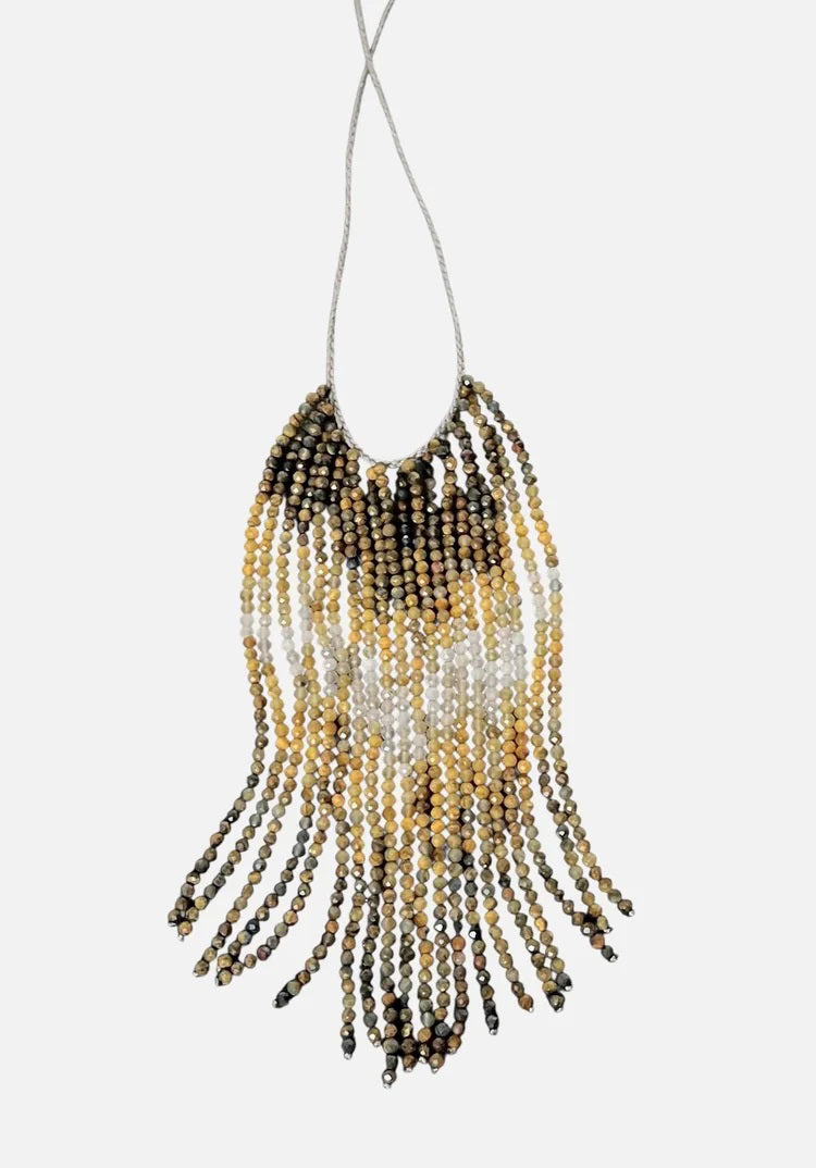 A mannequin wears a textured, curly taupe jacket and the ANN LIGHTFOOT Tiger Eye and Quartz Ombre Cascade Necklace, featuring dramatic dark beaded fringes in a triangular shape. The softly blurred background is neutral.