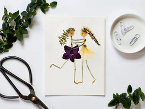 The "BEST FRIENDS CARD" by PETAL PEOPLE PRESS features two stick figures created from dried flowers and leaves, with one adorned in purple petals and the other in yellow. They appear to dance or embrace against a white background, making it an ideal choice for a pressed flower notecard or an elegant botanical art print.