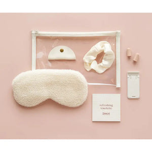 The PINCH PROVISIONS Travel Set is neatly presented in a transparent zippered pouch, designed for the contemporary traveler. Inside, you'll find a plush sleep mask, earplugs, cord organizer, phone/tablet stand, scrunchie, and a refreshing towelette. The packaging boasts a minimalistic design with "PINCH PROVISIONS - TRAVEL SET" and highlights the included 7 essentials.