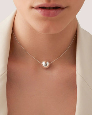 The JENNY BIRD - AURORA PENDANT NECKLACE by JENNYBIRD features a minimalist design with a sleek silver chain and a single high-polish silver bead at its center, elegantly suspended by a subtle slider closure against a plain white background.