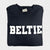 A black long sleeve tee shirt from the Fearrington Lifestyle Collection by Comfort Colors, crafted from premium fabric with the word "BELTIE" printed in large, bold, white capital letters on the front, neatly folded and laid on a white textured surface.