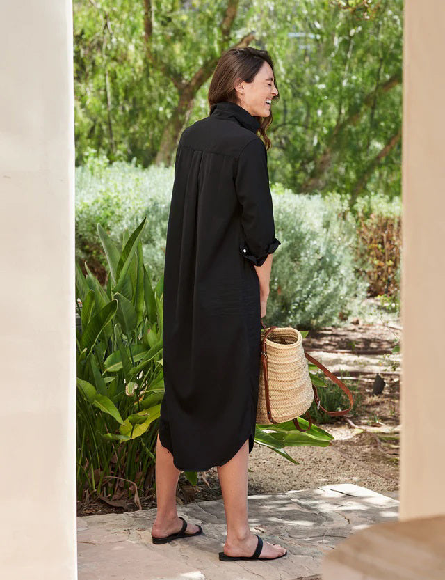 The dress is a FRANK &amp; EILEEN RORY Maxi Shirtdress in Famous Denim Black. It has a collar, rolled-up sleeves, a single chest pocket on the left side, and a curved hem. Crafted from fine Italian cotton, it is displayed against a plain white textured background.
