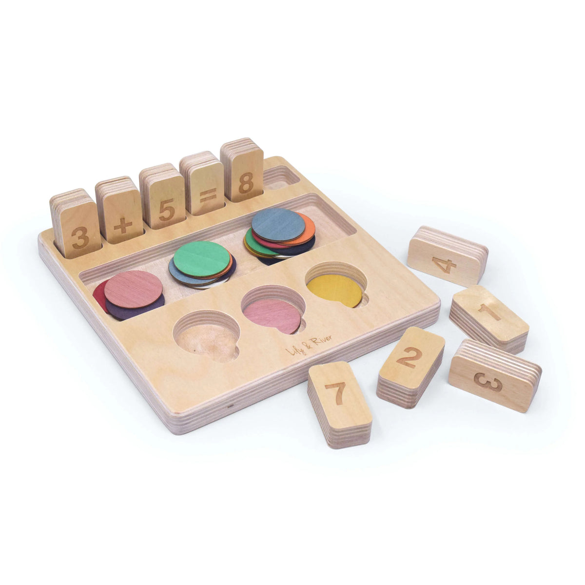 The &quot;LITTLE NUMBERS GAME SET&quot; by LILY &amp; RIVER is a wooden educational toy influenced by Montessori principles. It features number blocks and colored disks on a white surface. The blocks display a simple math equation (2 + 2 = 4), functioning like a children&#39;s calculator. In the background, there is a light-colored fabric bag with the text &quot;Lily &amp; River&quot; partially visible.
