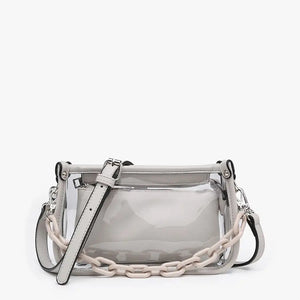 Introducing the CLEAR CROSSBODY BAG by JEN & CO: A stylish handbag crafted from vegan leather, showcasing a layered beige design with an open top and a visible zipper pocket. This bag is elegantly framed by a transparent outer layer and is complemented by a chunky beige chain strap for additional style and versatility.